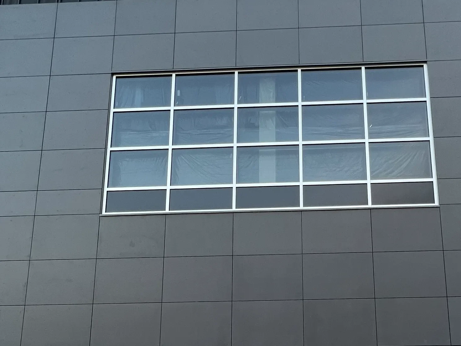Large-format dark grey fibre cement rainscreen panels around a glazed window grid