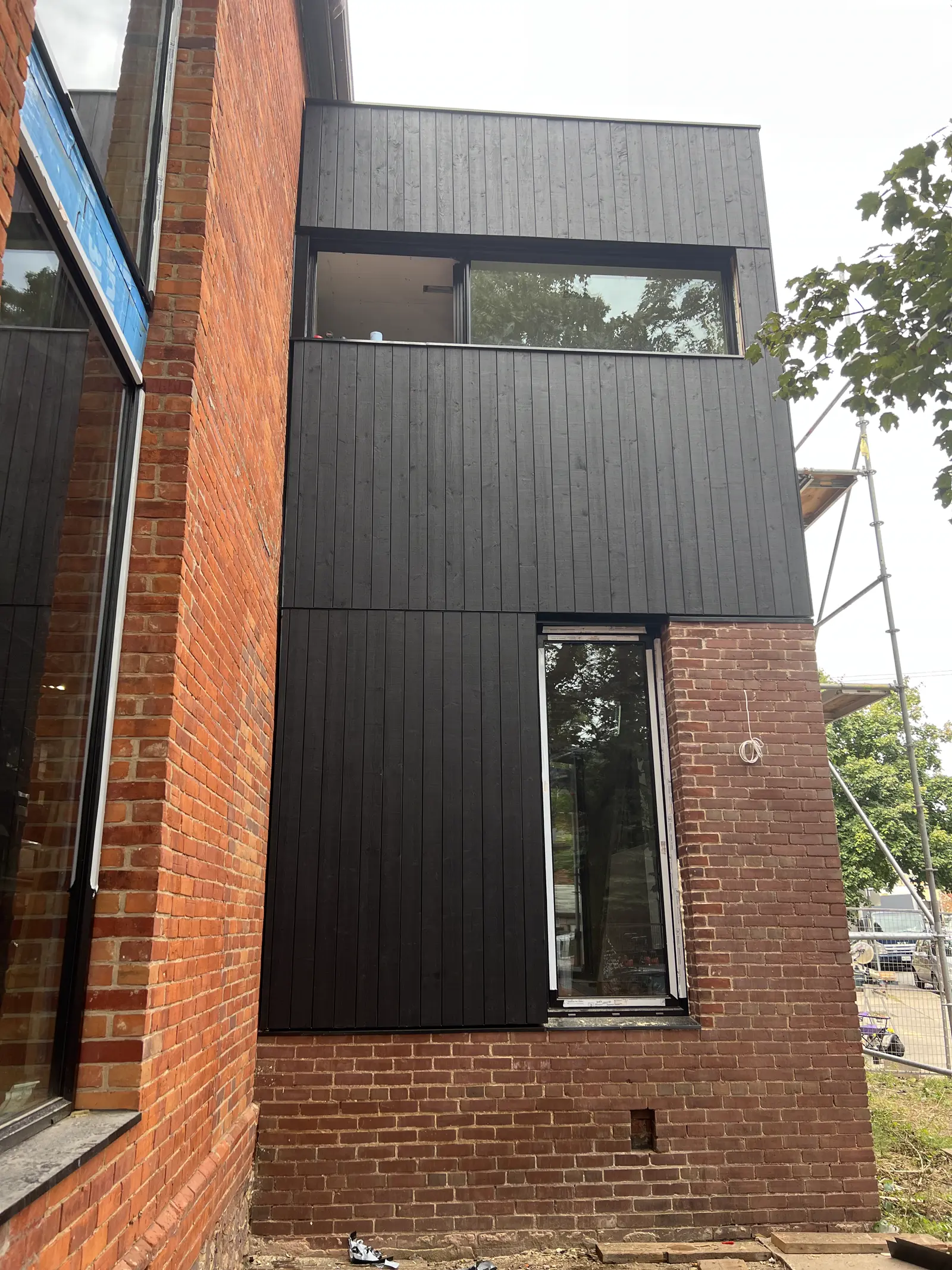 Dark vertical plank cladding meeting existing brick